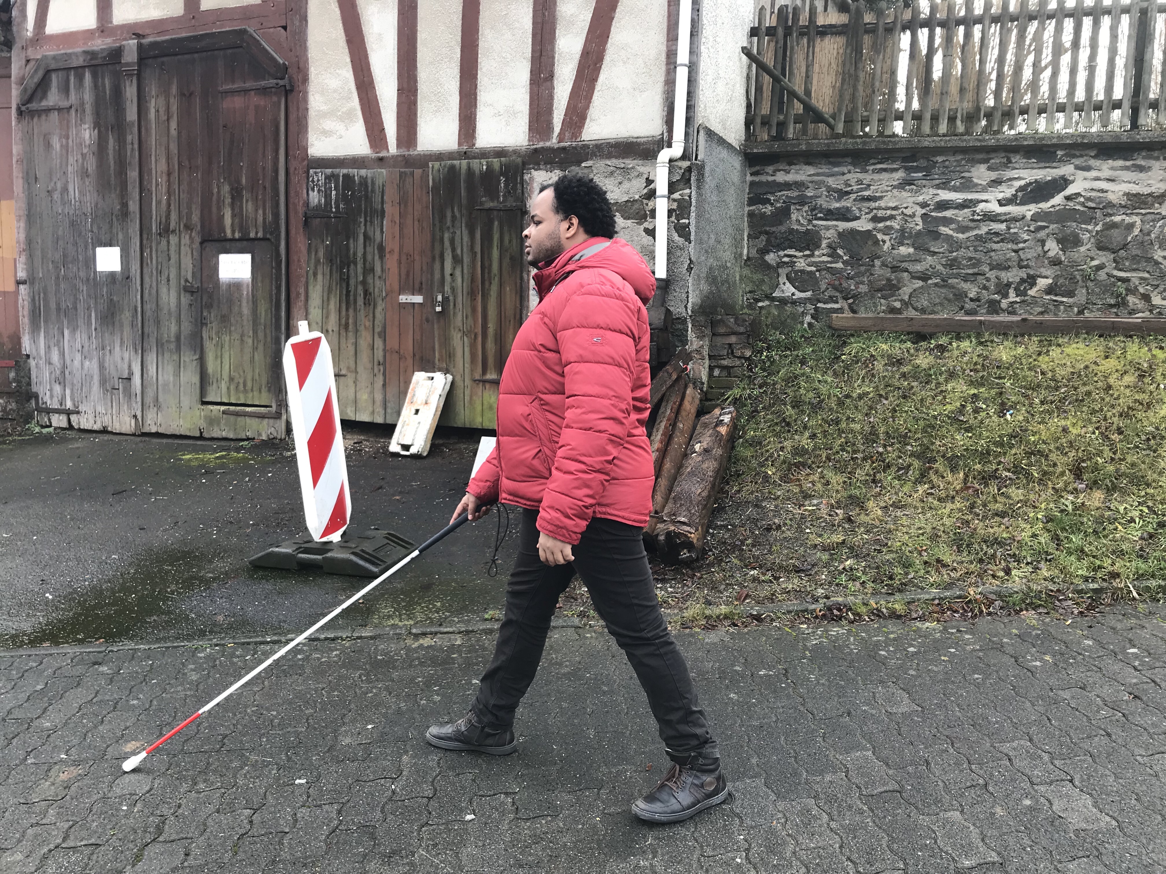 Mann, Der mit Blindenstock an einer Straße entlang läuft