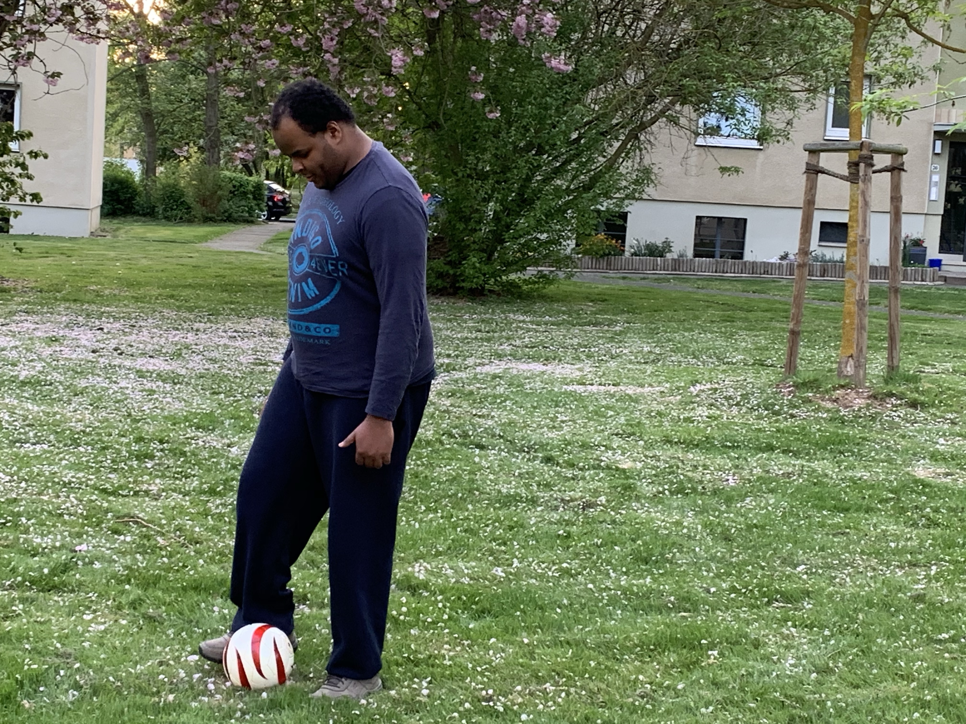 Johannes trippelt mit dem Blindenfußball auf einer Wiese mit Bäumen